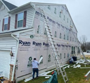 Workers siding a house with ladders and tools.