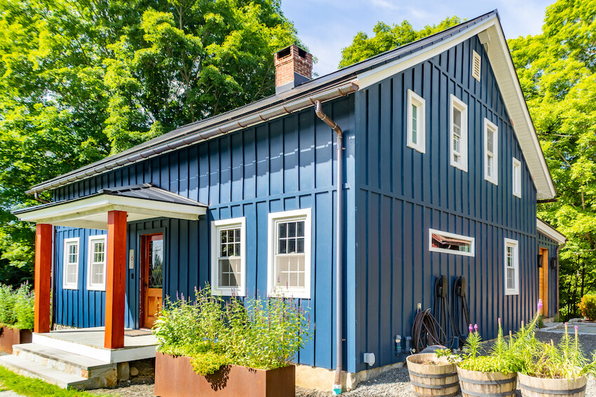 Blue farmhouse with large windows and green trees.