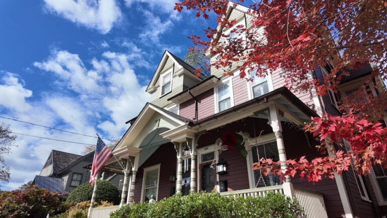 Victorian house with American flag and autumn leaves.