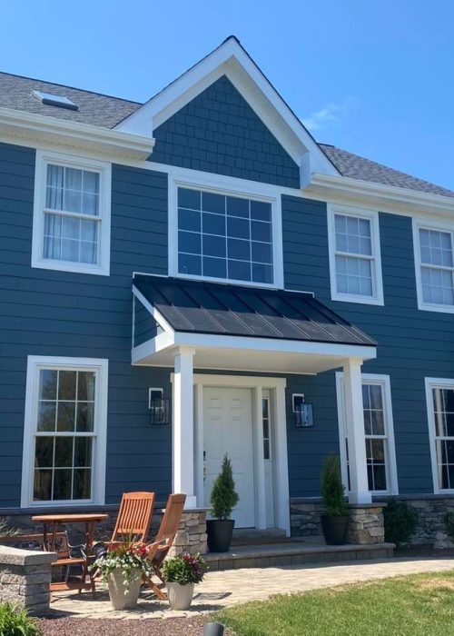 Blue two-story house with garden and patio chairs.